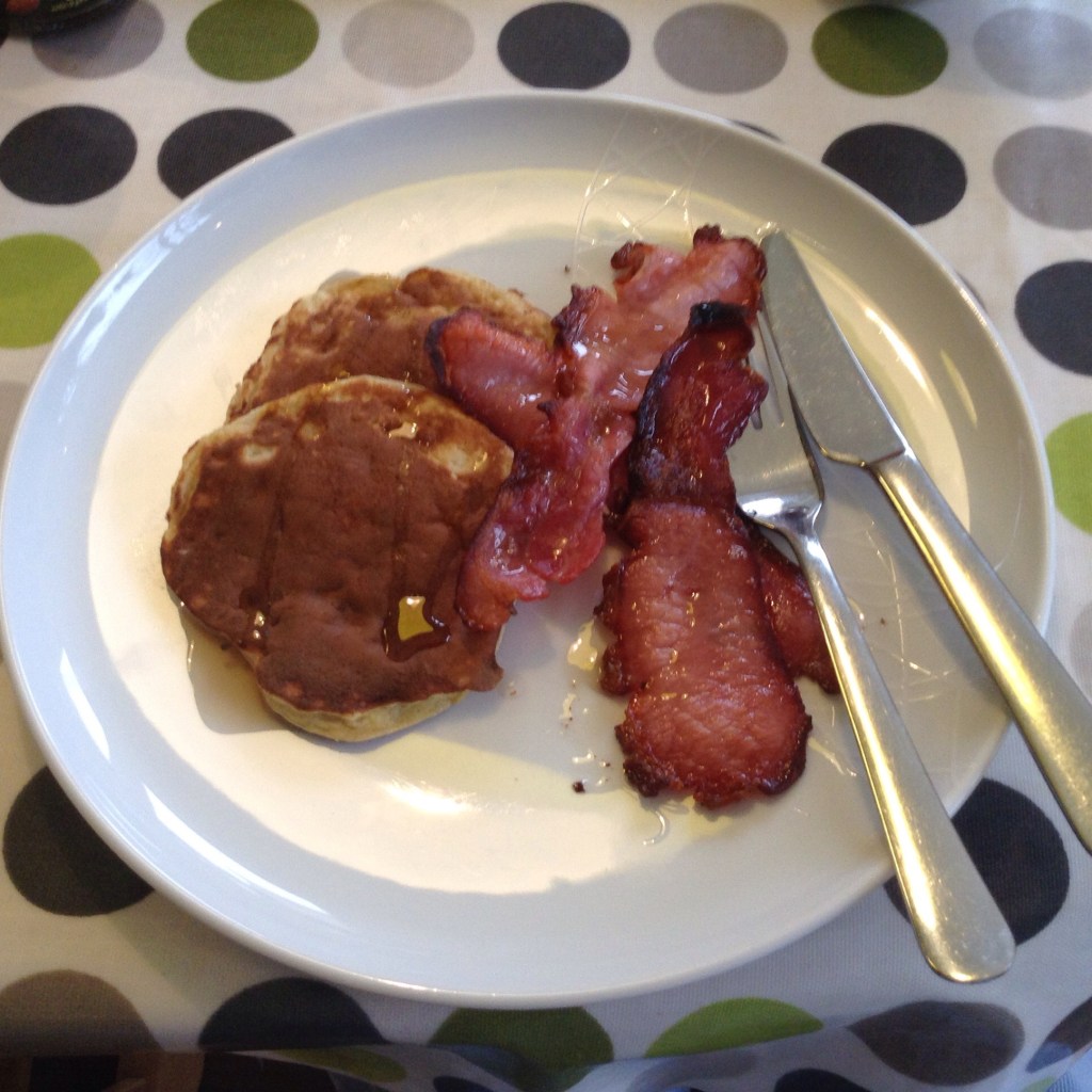 two banana pancakes with bacon, maple syrup and cutlery on a plate