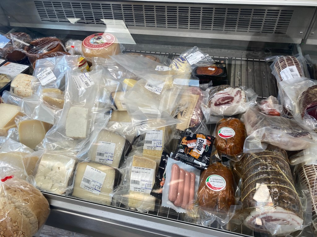 Delicatessen counter containing meats, and cheeses