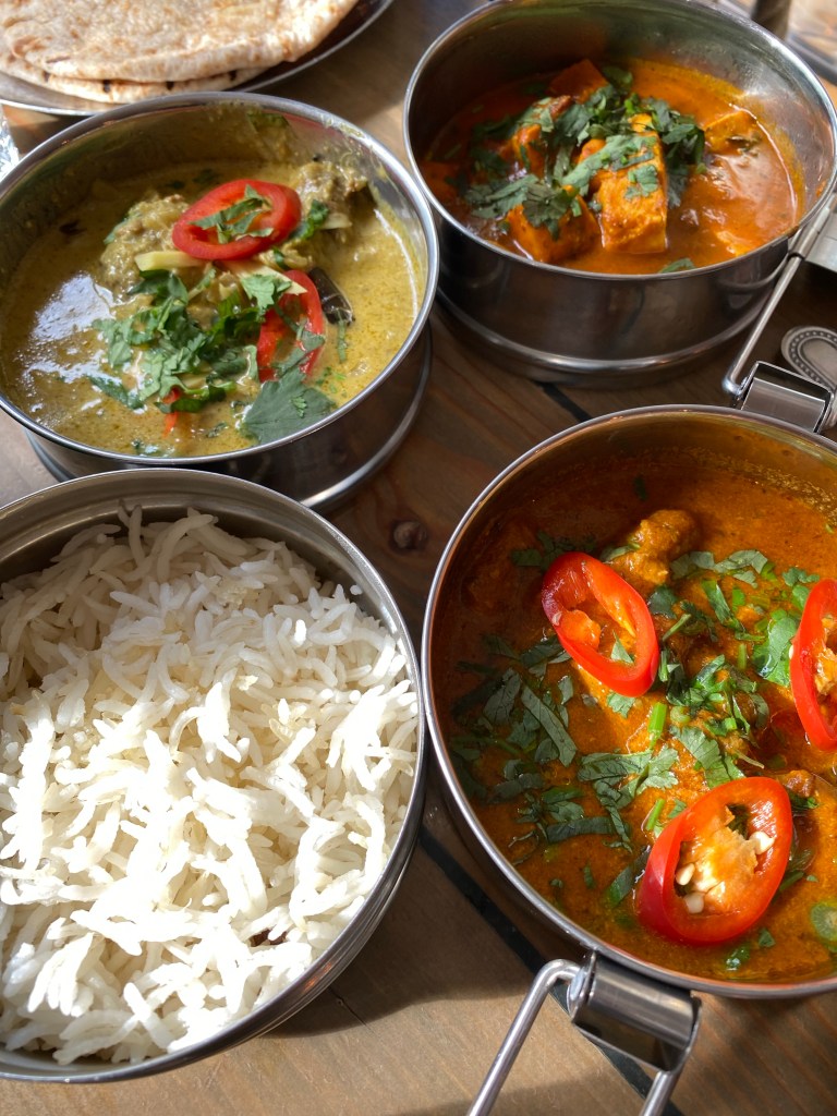 Four dishes of Indian food: rice, Keralan chicen curry, paneer and mother butter chicken