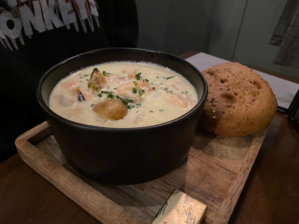 a bowl of chowder and some bread on a board
