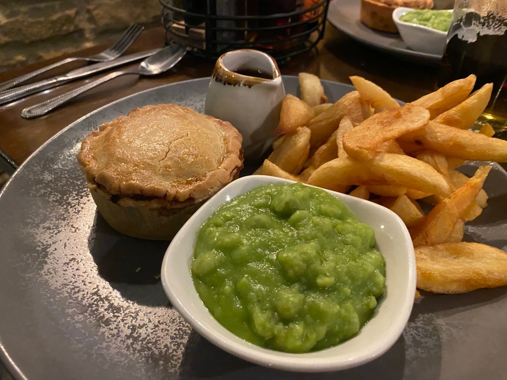 a big plate with a pie, thick chips, mushy peas and gravy