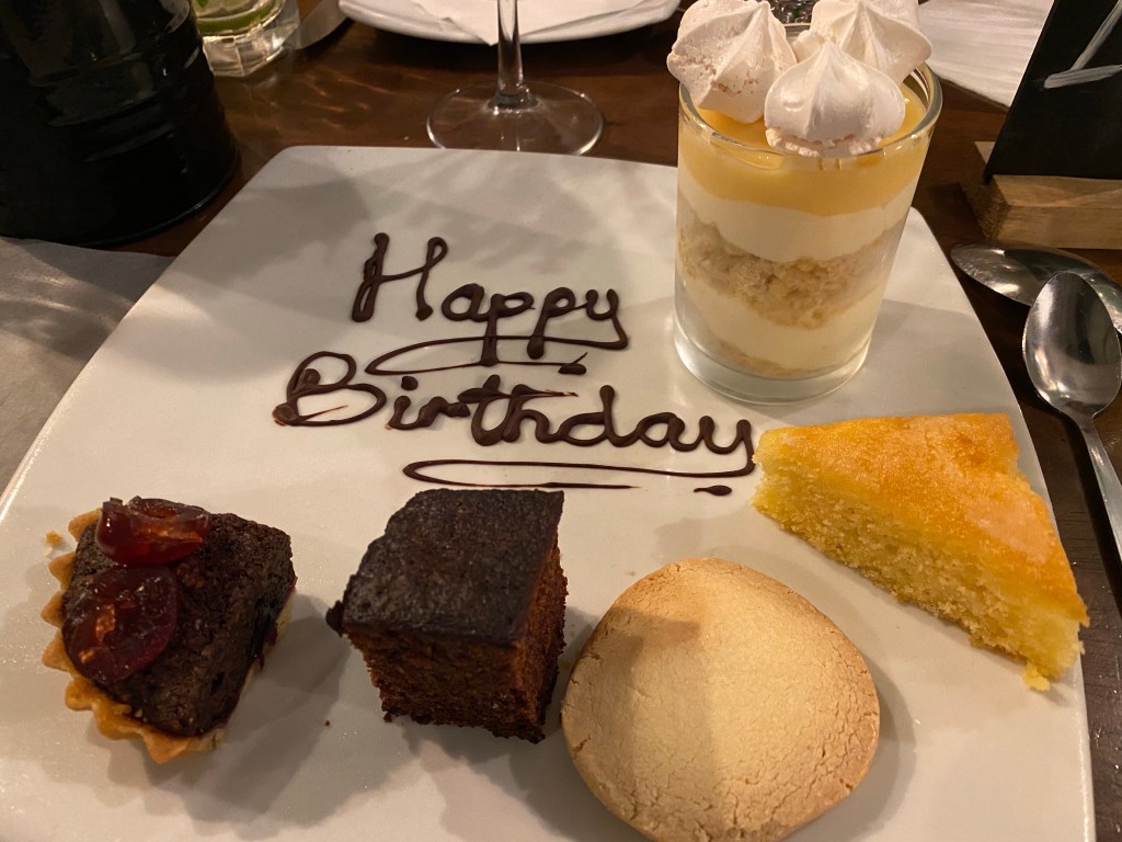 a big plate with happy birthday written in chocolate and five mini desserts on it