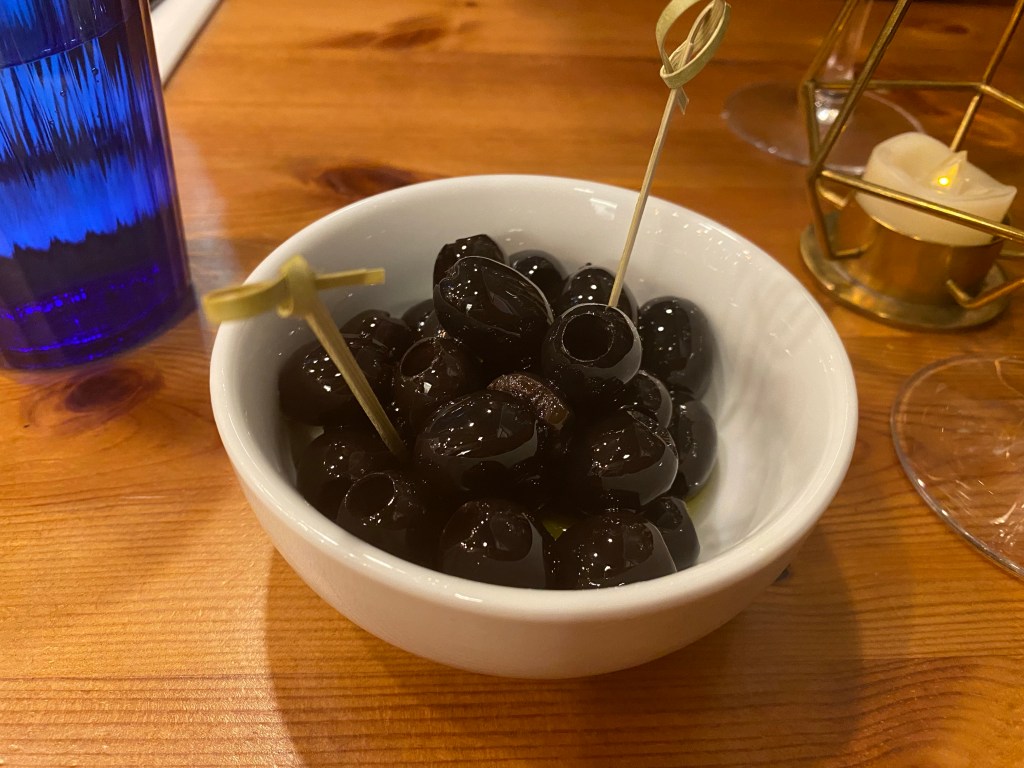 A bowl of black olives with two bamboo skewers