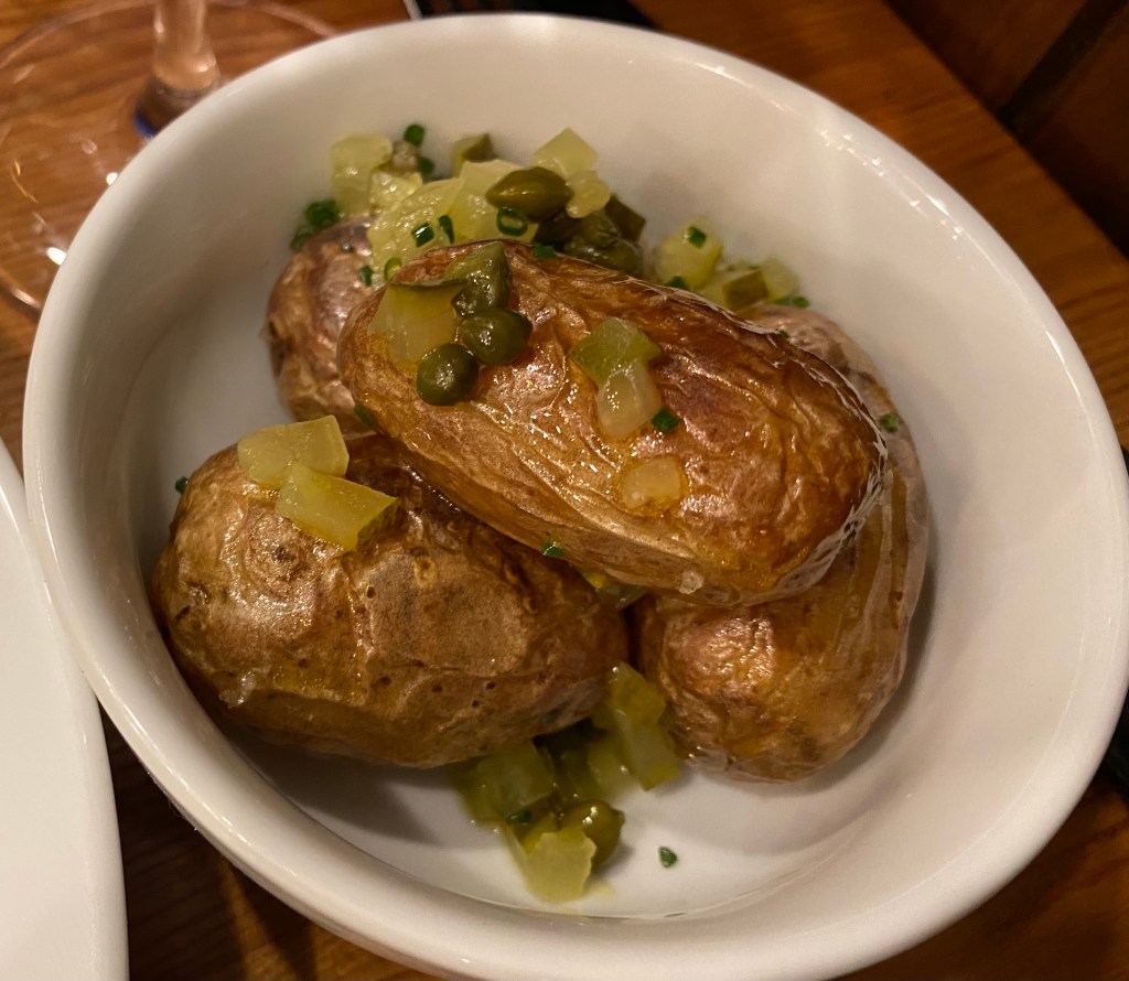 Small bowl of three potatoes with wrinkly skins and sprinkled with capers and chopped up gherkin