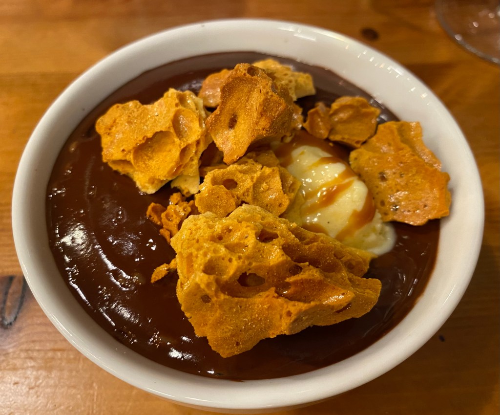 A small dish almost full to the brim with chocolate mousse and vanilla ice cream, covered with pieces of honeycomb 