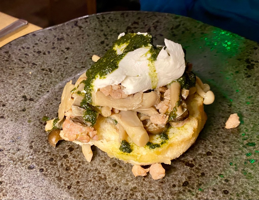 plate with wild mushrooms, bits of sausage, a mozzerella ball and pesto on a piece of crusty bread