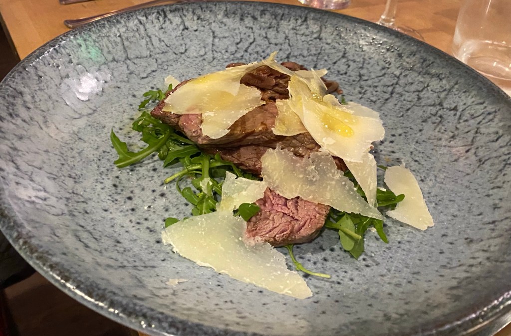 plate with slices of beef fillet on rocket, covered with pecorino cheese slices