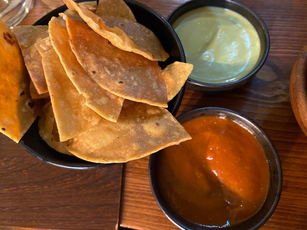 A bowl of crunchy taco pieces and two dips