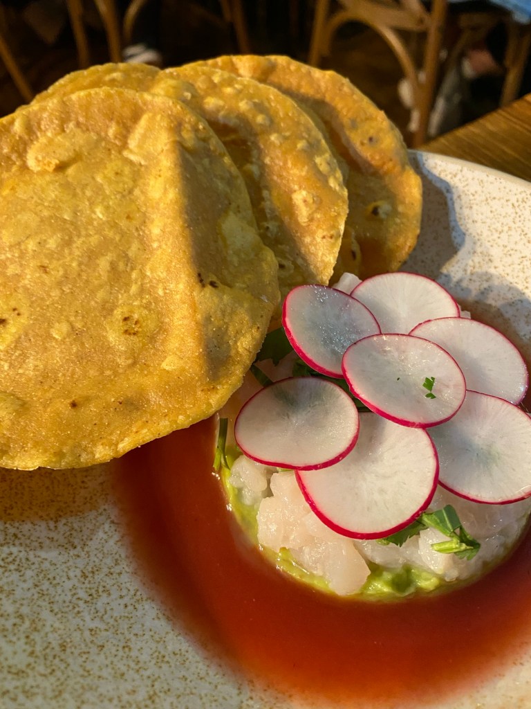 A dish with tilapia ceviche hiding under some sliced radishes, and even more crunchy tacos on the side