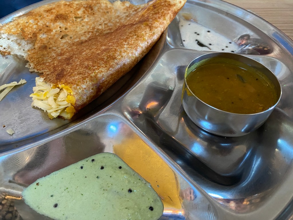 A paneer dosa on a metal tray with three sauces
