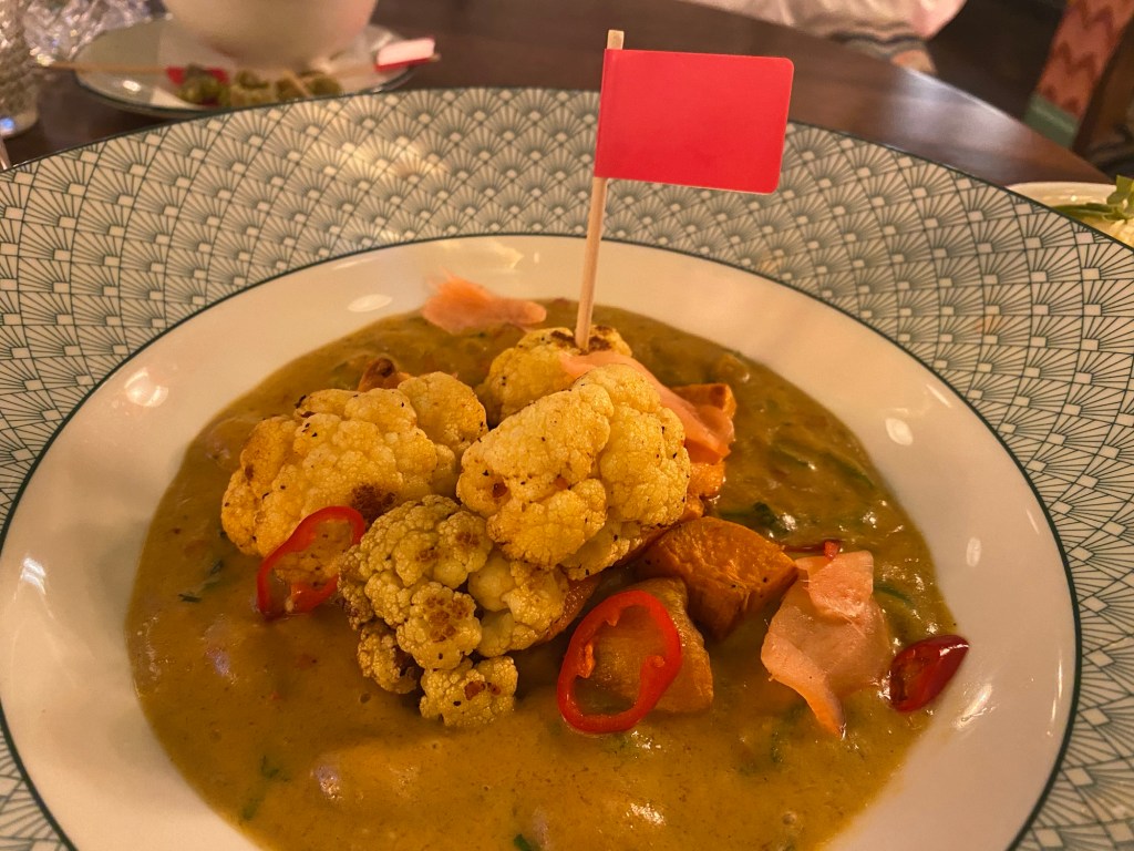 A bowl containing cauliflower Massaman curry with a red allergen flag in it
