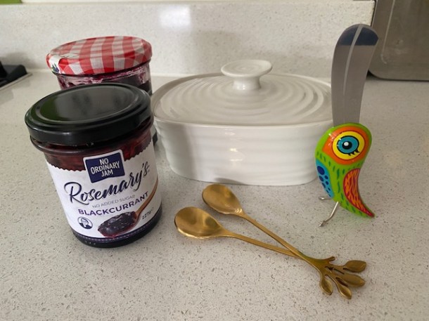 A butter dish and two pots of jam with a cute bird shaped butter knife and two, small, decorative spoons
