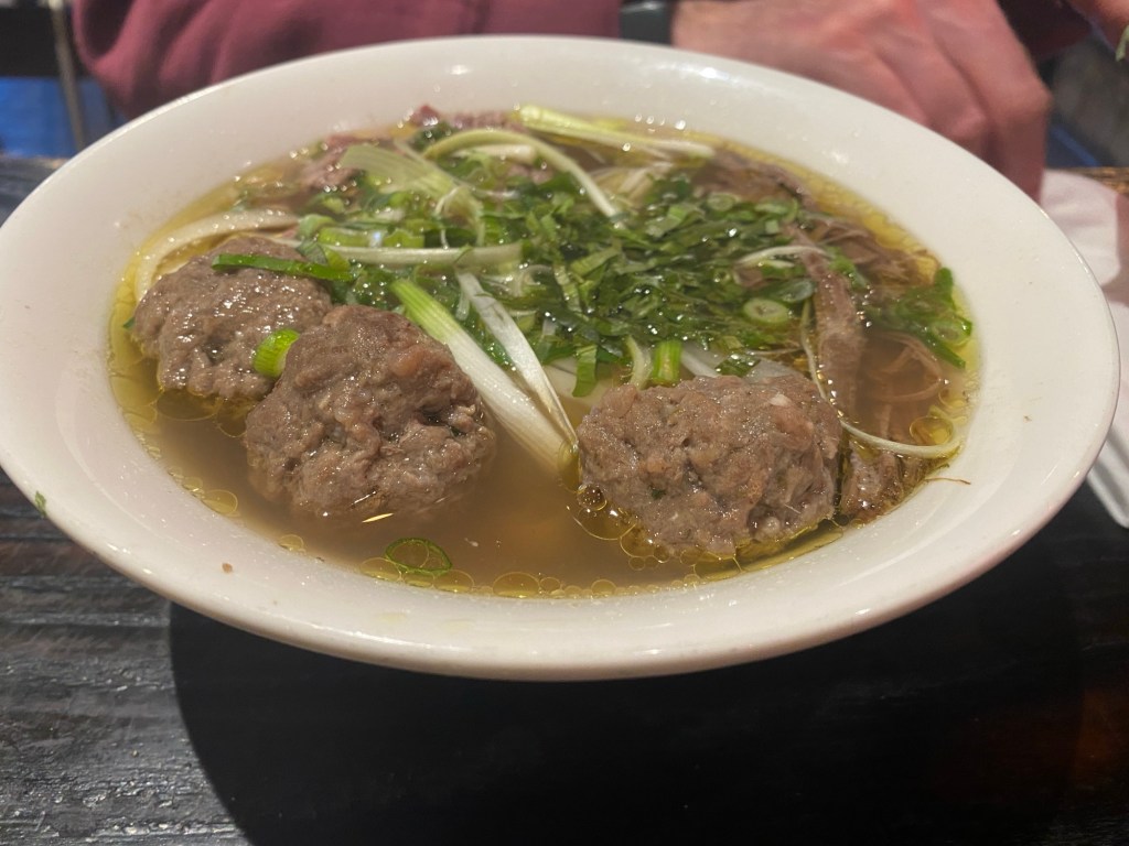 A large bowl of Pho soup with lots of meatballs bobbing around in it, and some herbs on the top