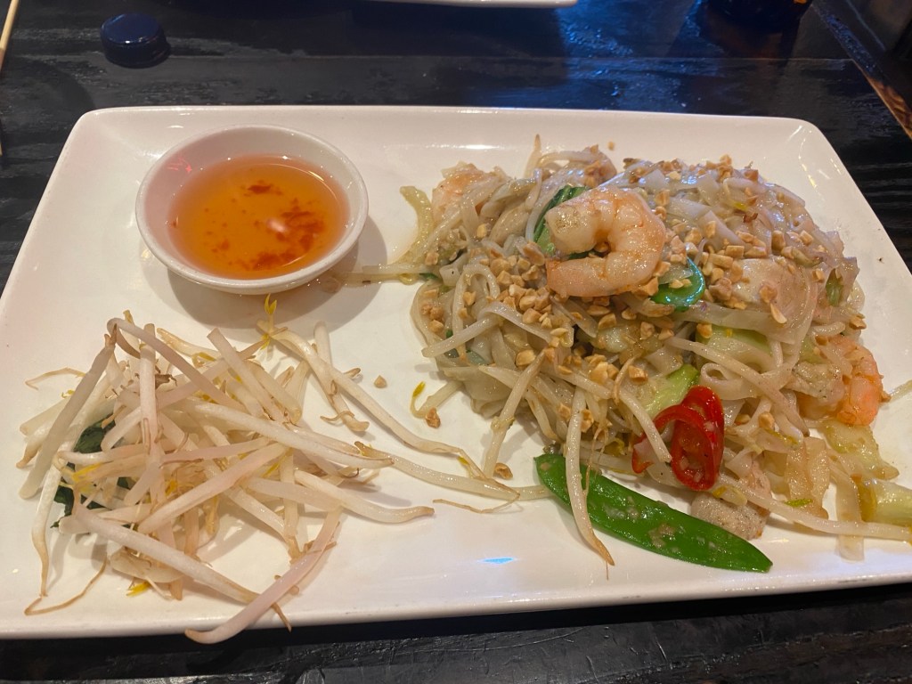large oblong plate with a prawn and chicken noodle stir fry, a pile of beansprouts and a bowl of dipping sauce