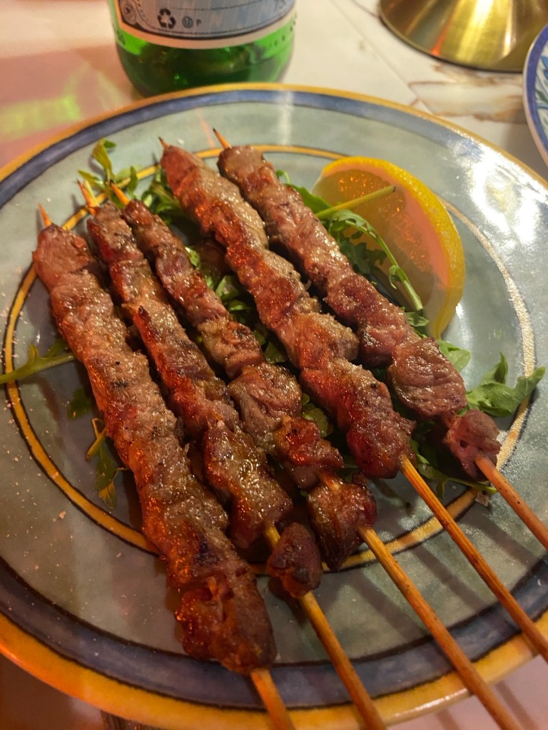a plate with five lamb skewers and a slice of lemon