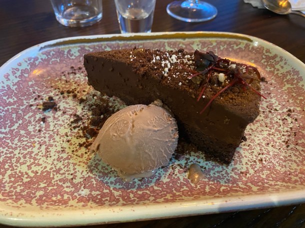 A pretty cream plate with pink splodges, with a piece of chocolate cheesecake (although it looks more like cake) and a scoop of chocolate ice cream.