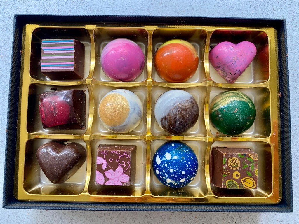 A rectangular box containing twelve really quite spectacular chocolates in different shapes (heart, sphere, square) and all brightly decorated with colours, prints and swirls